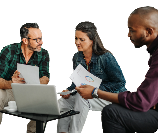 Team collaboration around a laptop: three professionals engaged in discussion, with a man in a green plaid shirt holding documents, a focused woman in denim attire reviewing papers, and another man in a burgundy shirt analyzing a report with graphs. The setting features a small black table, a coffee cup, and a productive brainstorming atmosphere.